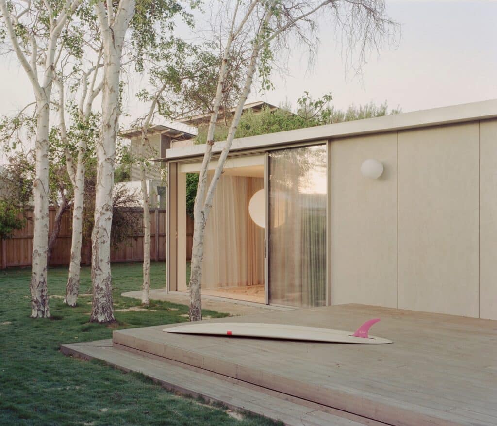 Exterior timber deck with a surfboard leaning against the house, showing the coastal lifestyle of the Wood House project.