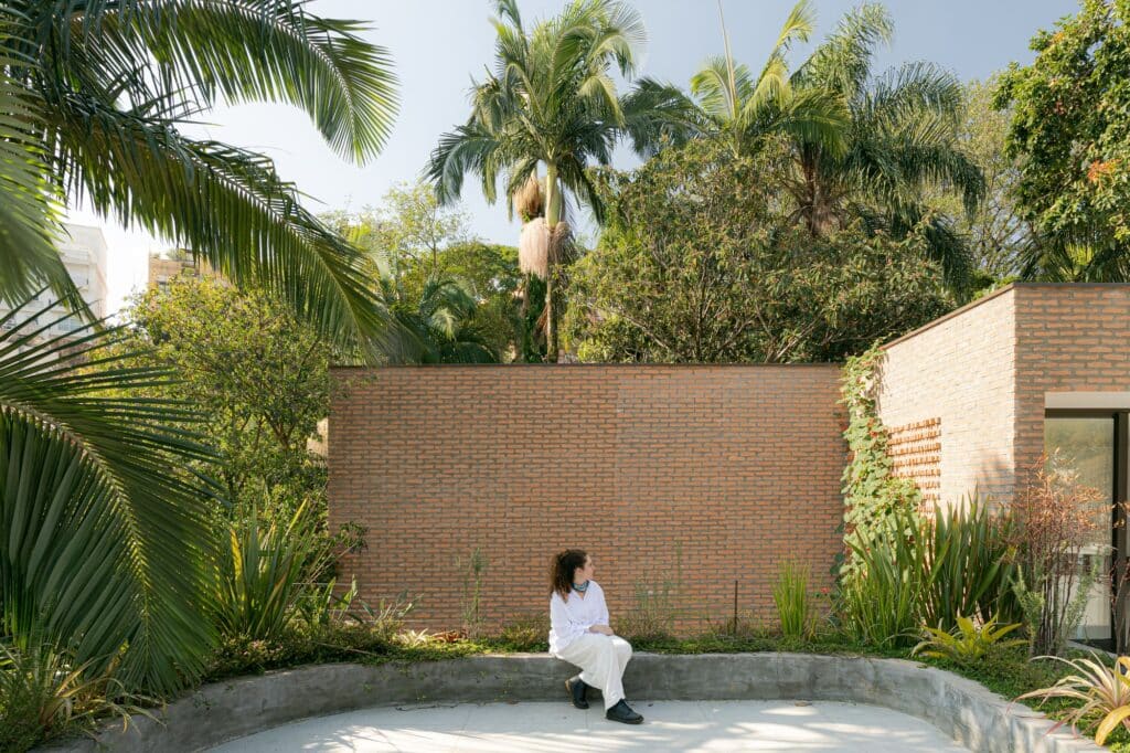 Rooftop terrace with a concrete bench, brick walls, and tropical trees in the background with a person sitting.