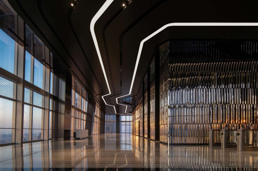 A panoramic sky lobby on the 34th floor featuring mirror-polished stainless steel walls and a wave-patterned ceiling overlooking the Jinan skyline.