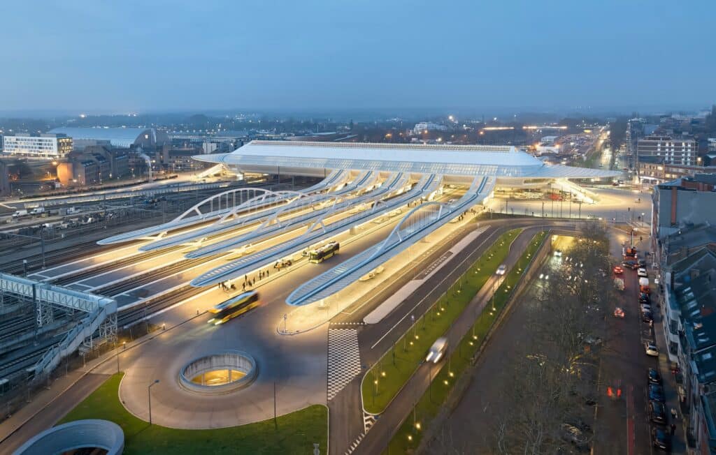 A wide dusk view of the integrated transit hub at Mons, showing the train station, bus terminal, and reorganized pedestrian areas.