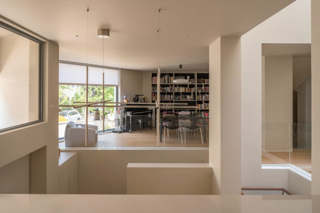 Interior view of a study and living area with large bookshelves, a piano, and a wide window overlooking trees.