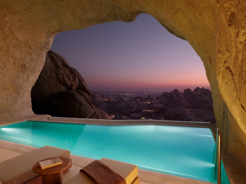 Interior of a luxury suite carved into a rock cave with a private infinity pool overlooking the desert at sunset.