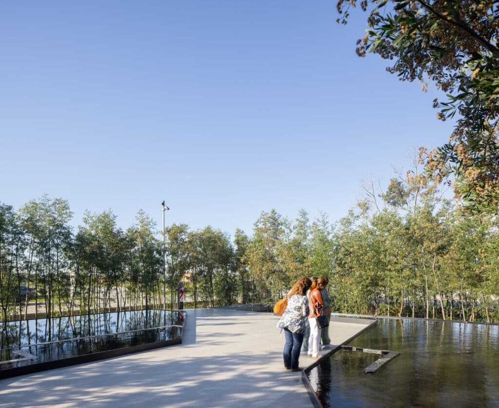 Visitors standing by a minimalist black-edged reflecting pool within the Malba Puertos botanical area.