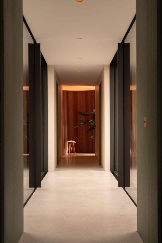 Minimalist interior hallway with glass walls and a view of a cylindrical wooden feature at the end.
