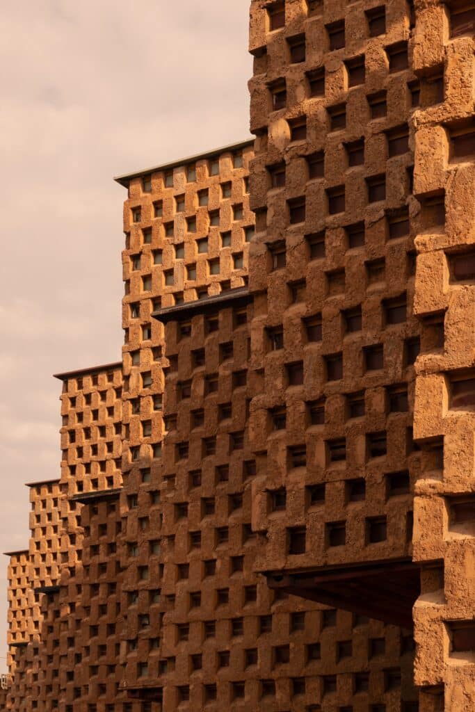 Architectural detail of the staggered mud-covered container modules against a cloudy sky.