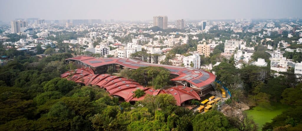 Aerial view of Shiv Nadar School Chennai showing the red corrugated roof with solar panels integrated into a lush green urban landscape.