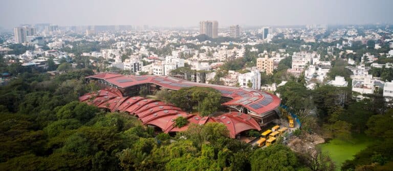 Aerial view of Shiv Nadar School Chennai showing the red corrugated roof with solar panels integrated into a lush green urban landscape.