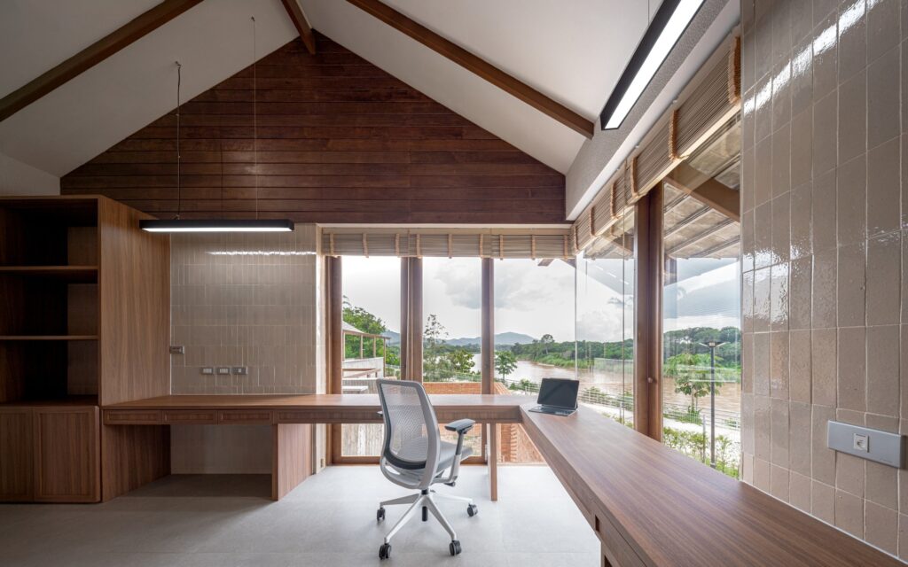 Minimalist home office interior with a long wooden desk and a panoramic window facing the river.