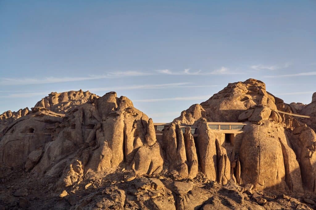 Close-up of villa units seamlessly integrated into the golden cliffs of the Hijaz mountains under a clear blue sky.