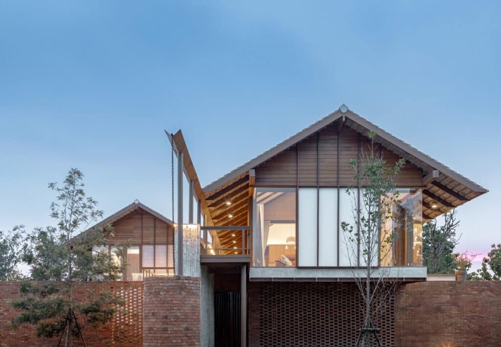 Night view of Baan SudSaenSuk with warm interior lighting highlighting the "fa lai" sliding wood panels.