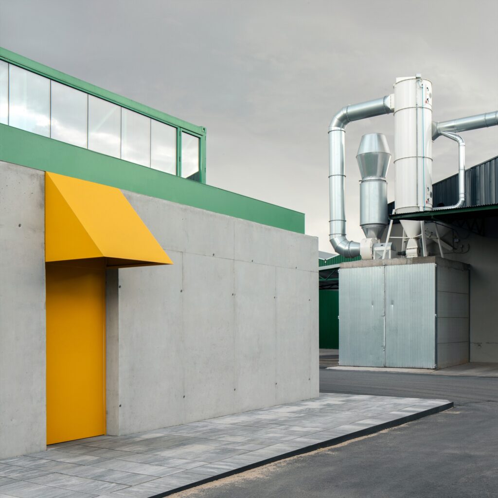 Close-up of a concrete wall with a yellow door and matching yellow metal awning next to industrial machinery.