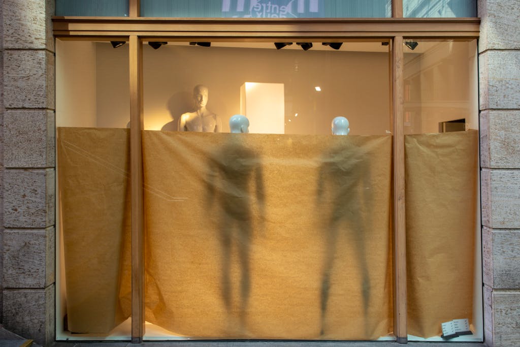 Store display with mannequins partially concealed by brown paper cover in a window.