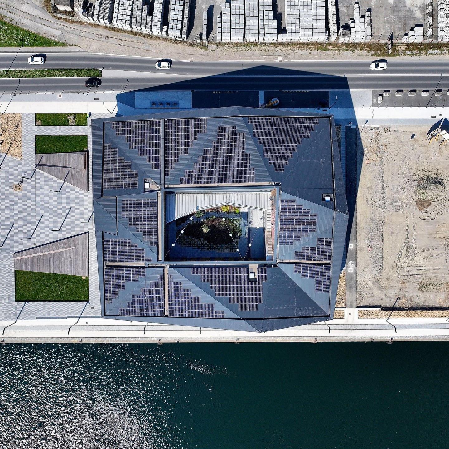 The Écosystème D energy-positive building in Dunkirk, France, viewed from across the water at dusk, with its lights reflecting on the surface.