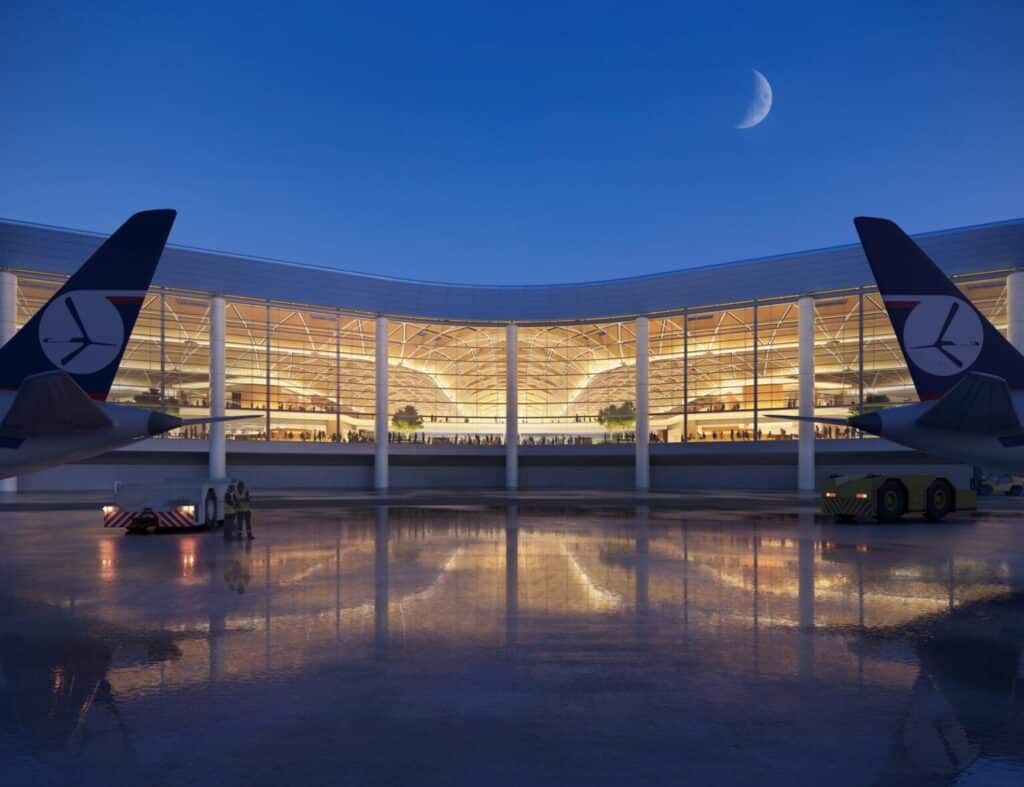 A night rendering of the Poland new airport terminal from the tarmac, showing a glass facade and arched wooden interior structure.