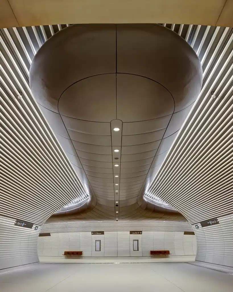 Passengers walking through curved white archway inside Gadigal Metro Station with ribbed ceiling panels and Bathurst Street wayfinding signage