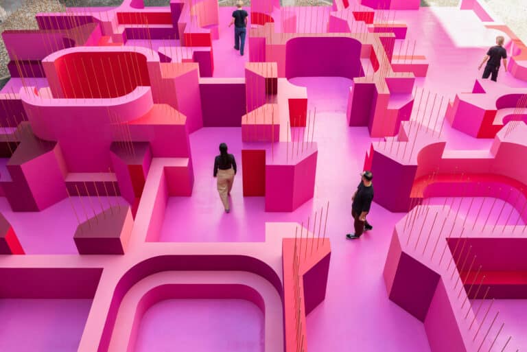 Visitors walking through a vibrant pink labyrinth in a historic courtyard