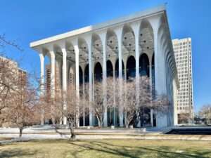 Modernist facade of the Philip Johnson-designed New York State Theater at Lincoln Center, featuring tall white arches and vertical marble panels.