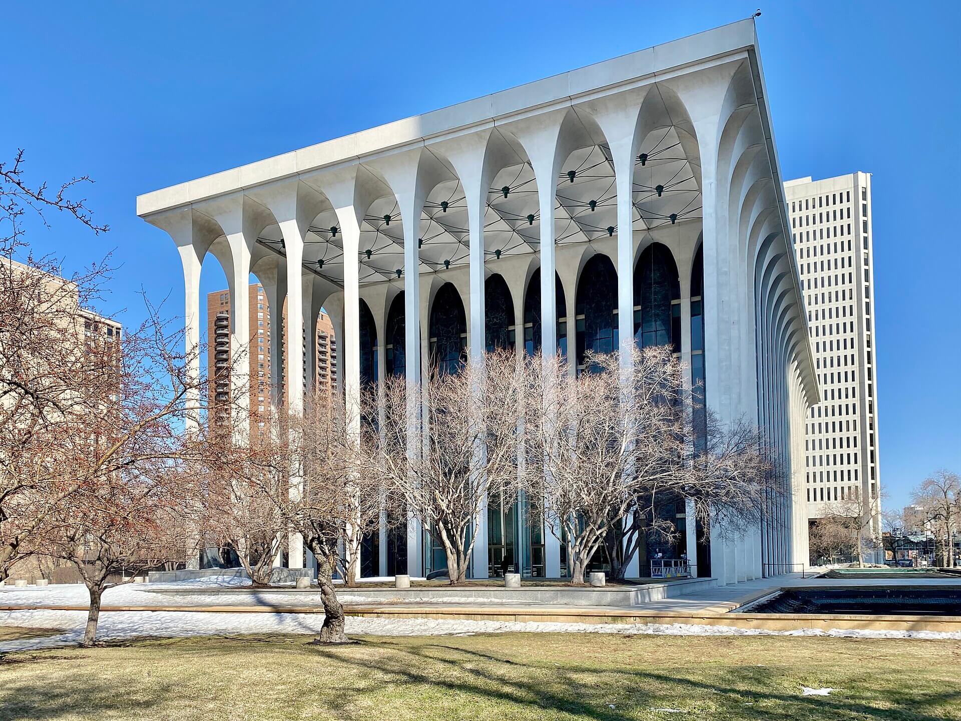 Modernist facade of the Philip Johnson-designed New York State Theater at Lincoln Center, featuring tall white arches and vertical marble panels.