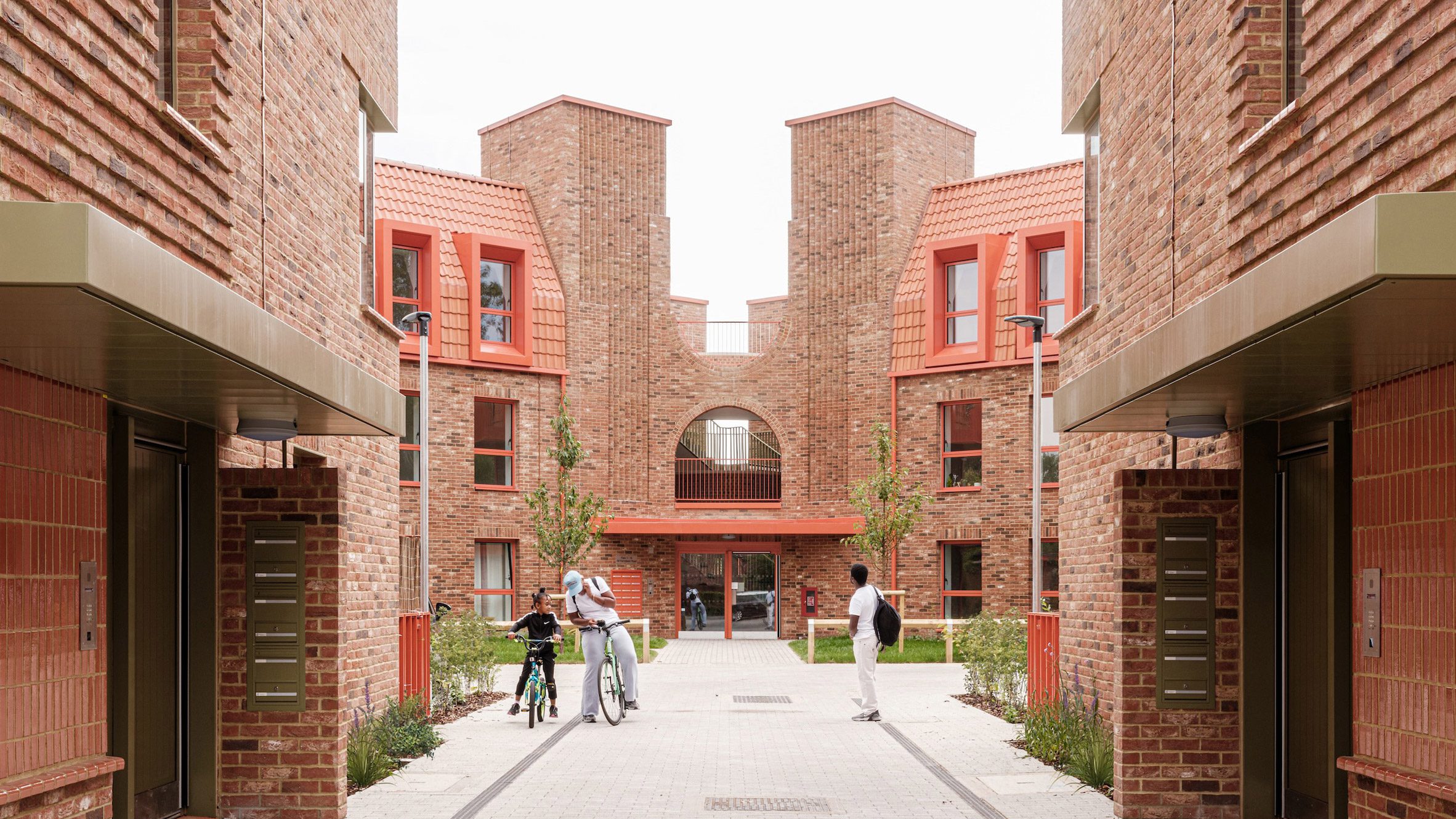 Brick balcony with orange metalwork balustrades and textured chimney towers at Farmstead Road affordable housing London