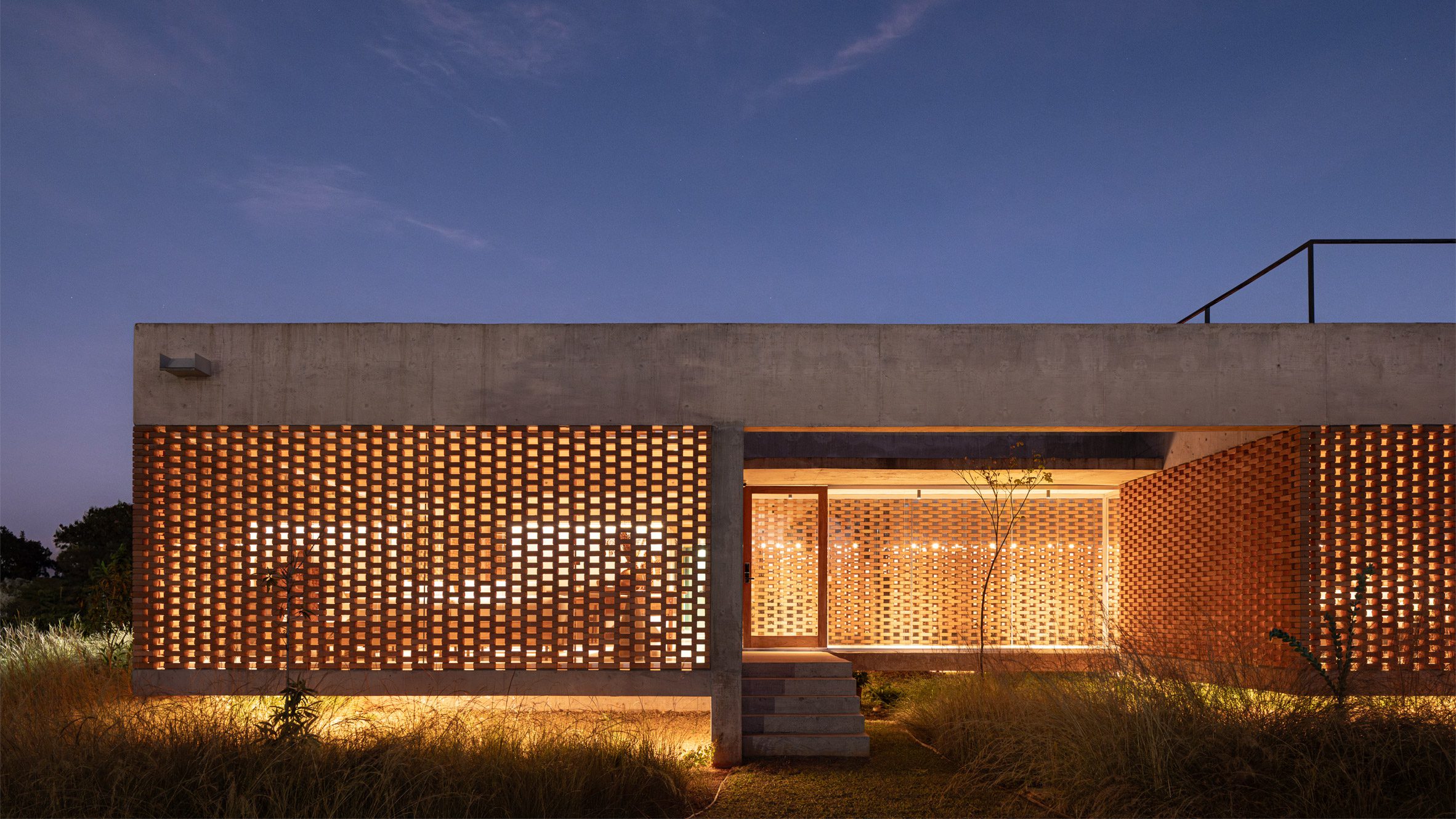 Perforated brick screens glowing at night on Casa Tupin windowless house in Brasília