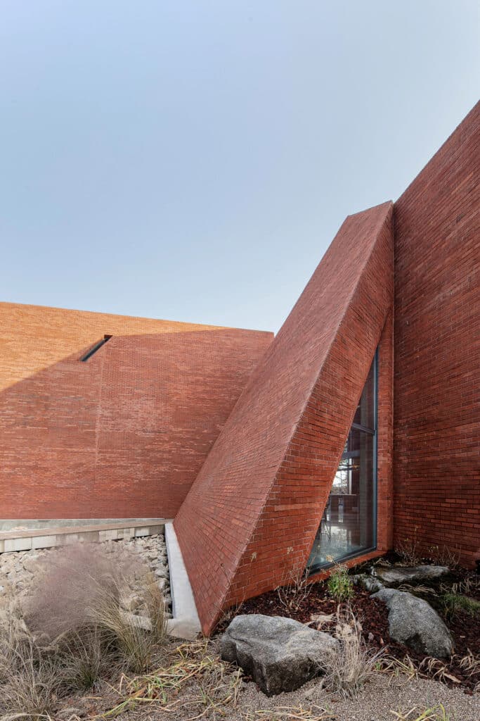 Abogoga cafe red brick facade with angular opening and rocky landscape