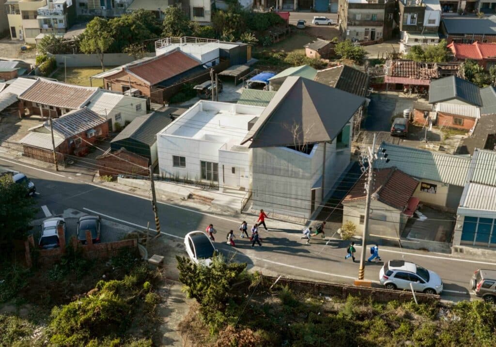 Aerial view of Tianlai Art Museum showing its exposed concrete exterior and asymmetrical hat-shaped roof among rural village houses.