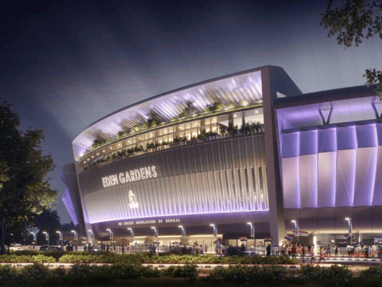 Night exterior view of Eden Gardens stadium facade with illuminated entrance and landscaped frontage