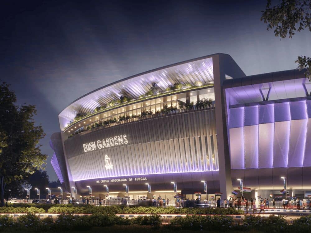 Night exterior view of Eden Gardens stadium facade with illuminated entrance and landscaped frontage