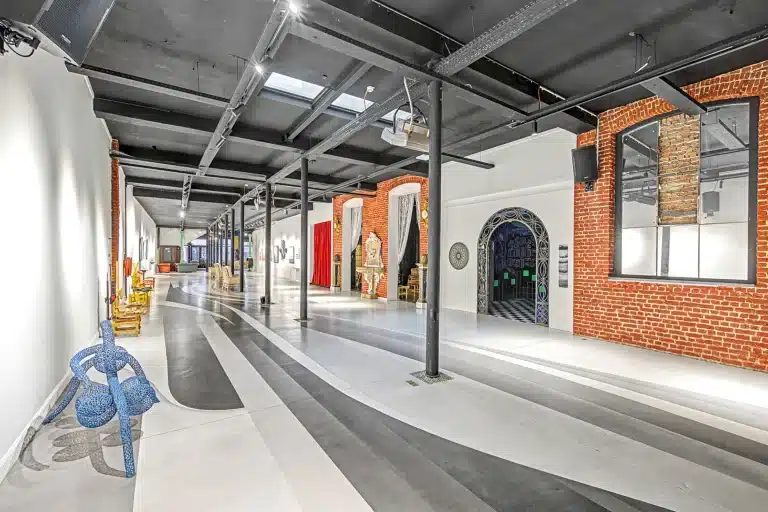 
قاعة العرض داخل مصنع بروكسل تتميز بجدران من الطوب المكشوف وعوارض سقف معدنية سوداء