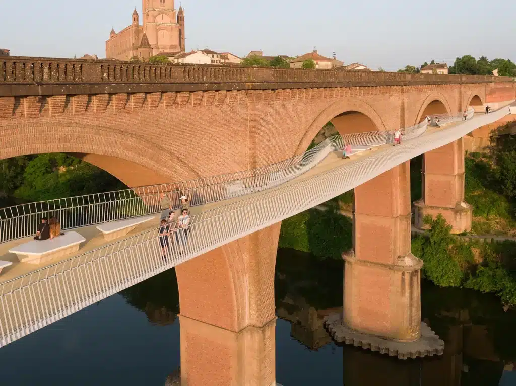Aerial view showing the waving path of the steel footbridge parallel to a straight historic railway viaduct over a river.