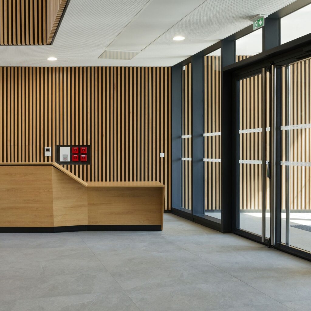 الفناء المركزي المفتوح في مبنى إيكوسيستيم دي الإيجابي للطاقة، مع مساحات خضراء وممرات وإطلالات على الواجهات الخشبية المحيطة.