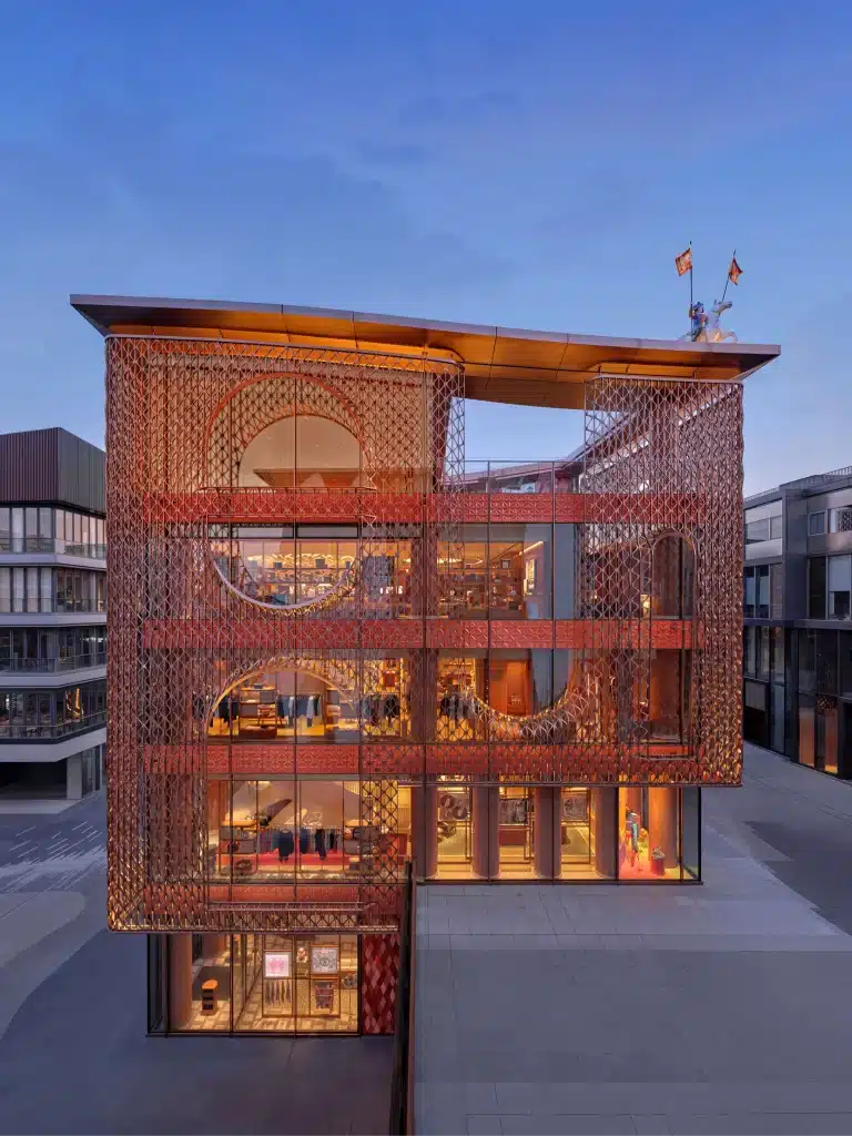 The ceramic facade of the Hermès Beijing flagship at dusk, with warm light glowing from the interior through the screen.