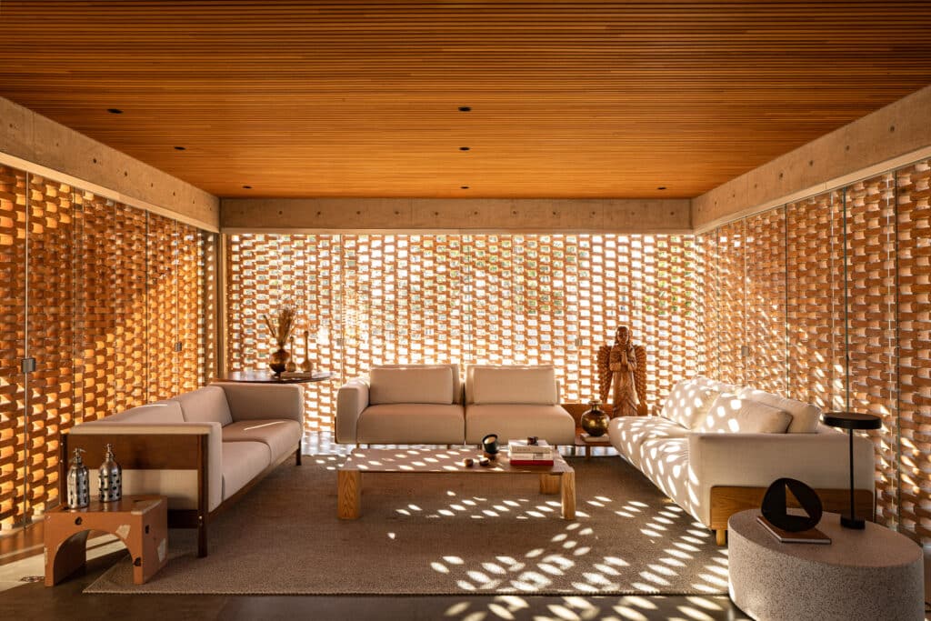 Filtered light patterns through perforated brick walls in Casa Tupin living room with timber ceiling