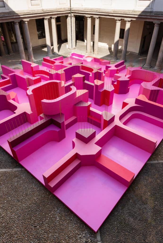 Aerial view of a modular pink labyrinth made of wood in a stone courtyard