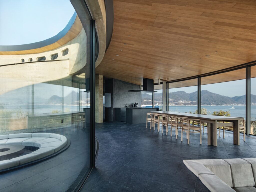 لقطة علوية مقربة لفناء داخلي يتميز بجدران ترابية منحنية ومسبح وحفرة نار دائرية غائرة.