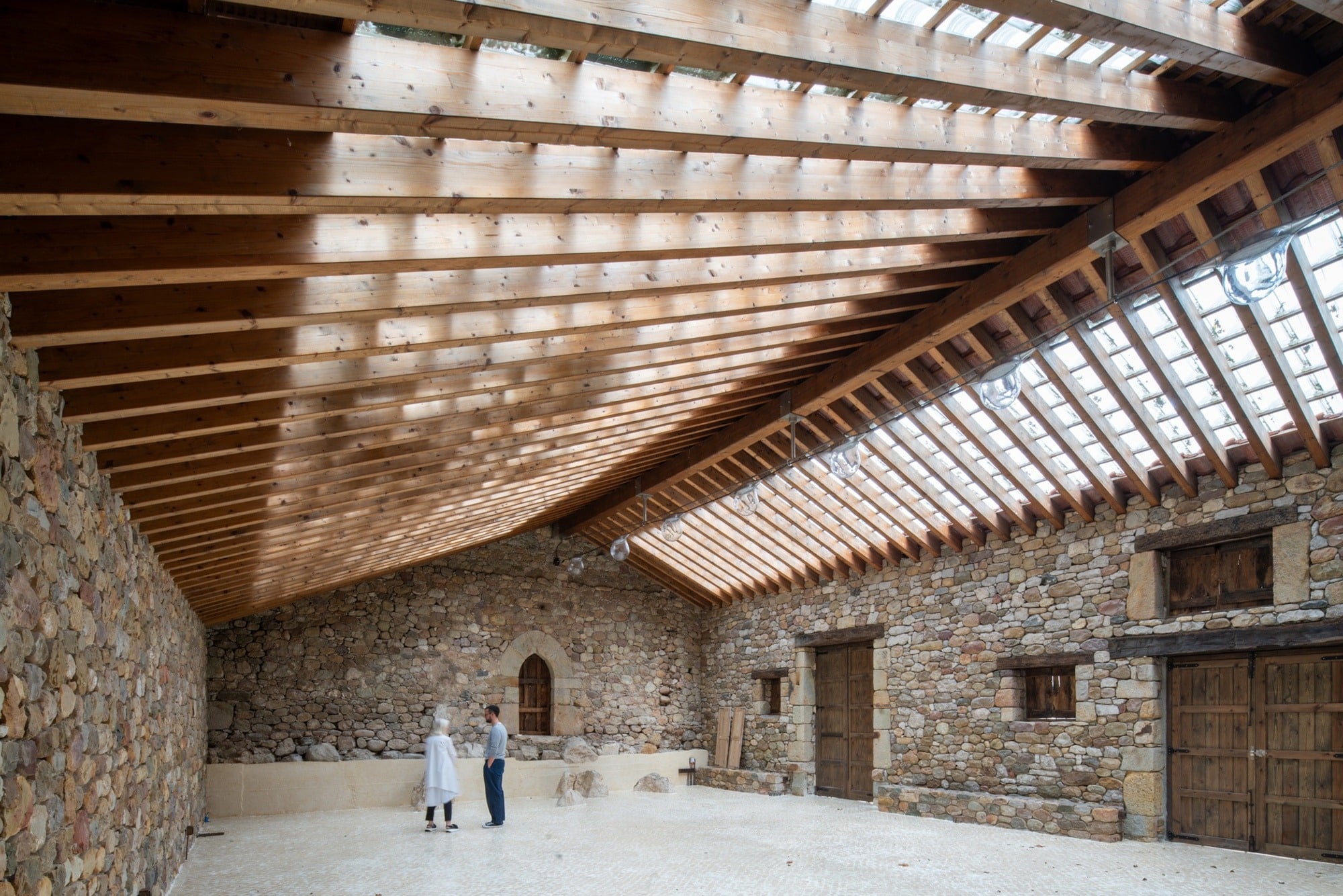 Interior wide view of Tiled Sky Pavilion showing the wooden roof structure, glass tiles filtering natural light, and original stone walls.