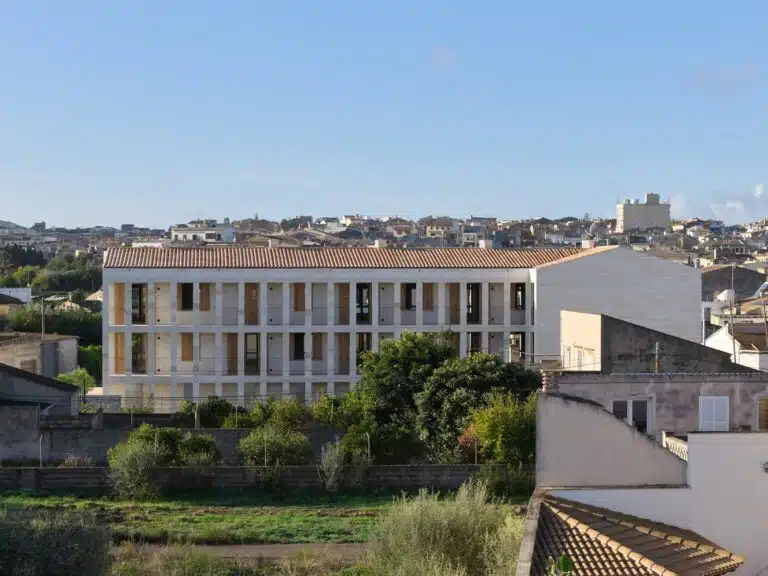 Exterior view of the Santa Margalida social housing building featuring a local Mares stone facade and integrated balconies under a clear blue sky.