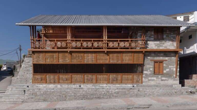Side elevation of Champawat Market Plaza featuring local stone walls and a modular wooden balcony with woven bamboo screens.