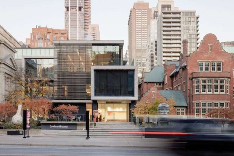 Exterior facade of the Gardiner Museum in Toronto showing the 1983 limestone building and 2006 expansion during dusk.