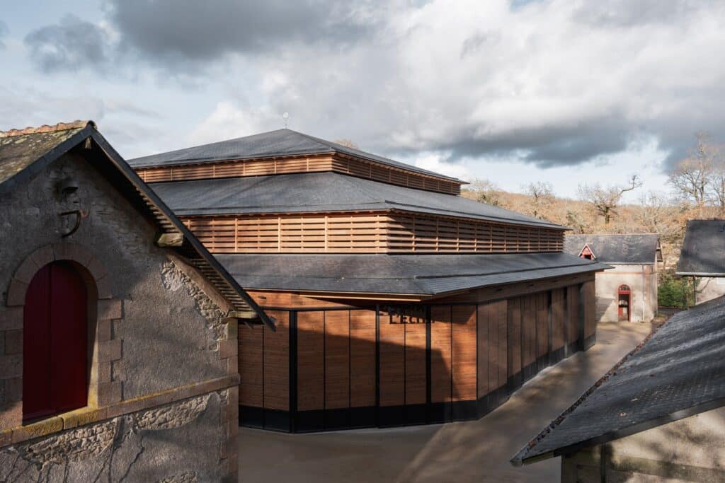 Exterior view of the Hennebont equestrian performance hall showing the tiered slate roof and timber louvers integrated within the historic Haras National courtyard.