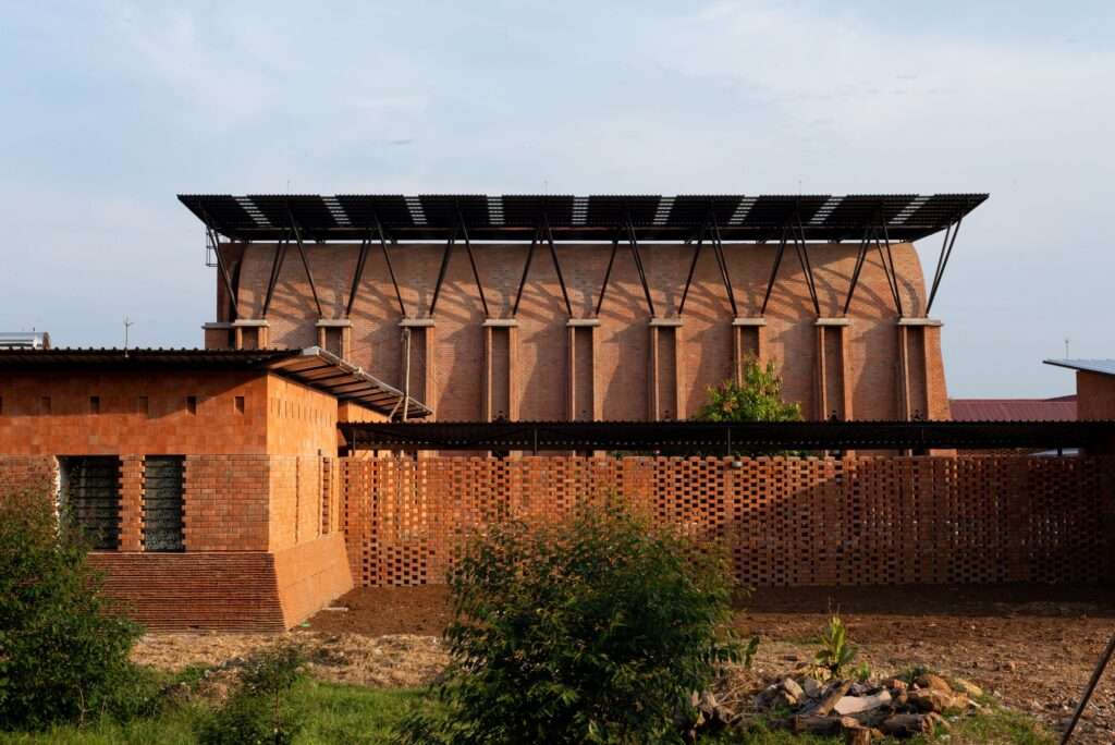 Exterior view of Our Lady of Victory Abbey expansion in Kenya featuring clay brick walls and a secondary tropical roof for shading and solar panels.