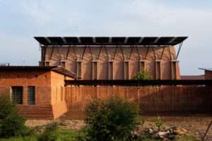 Exterior view of Our Lady of Victory Abbey expansion in Kenya featuring clay brick walls and a secondary tropical roof for shading and solar panels.
