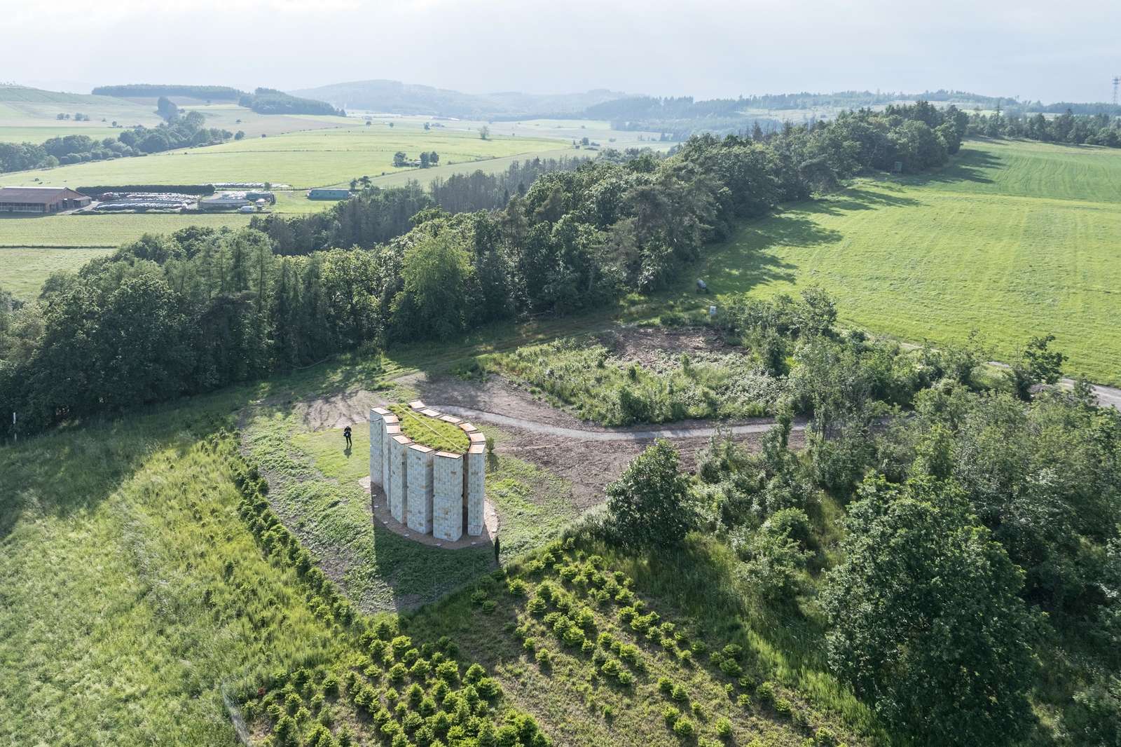 Aerial view of the Open Chapel in Hillerhausen, Germany, featuring twelve sandstone columns on a green hilltop surrounded by forests and fields.