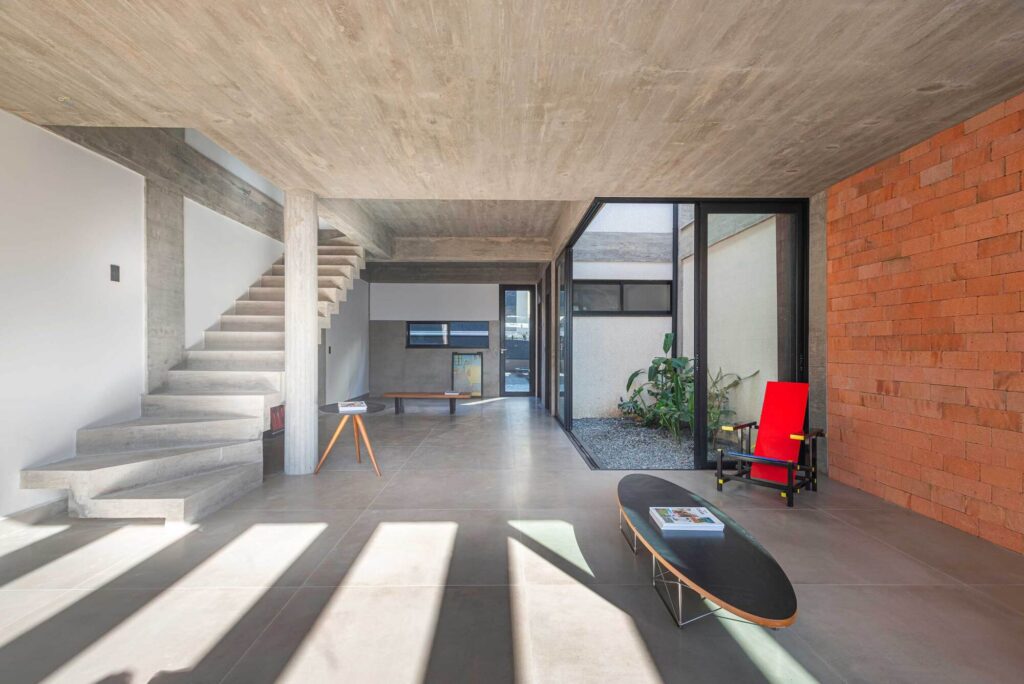 Minimalist living room with internal courtyard, exposed concrete ceiling, and orange brick wall.