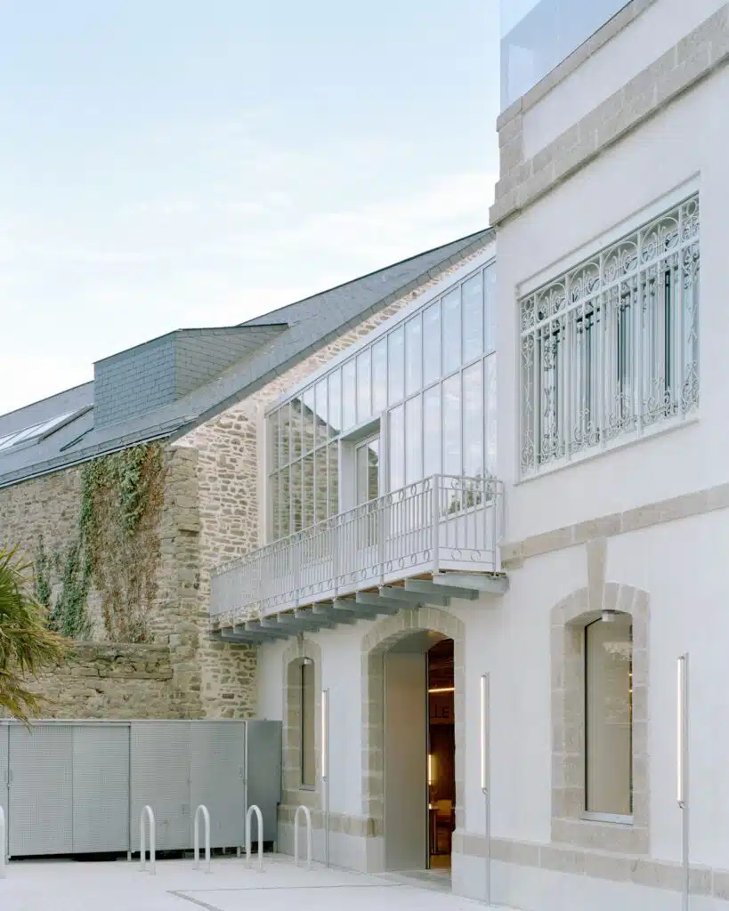 Close-up of the glass winter garden and outdoor balcony area in the Maison FLOW project, featuring original stone walls and modern steel railings.