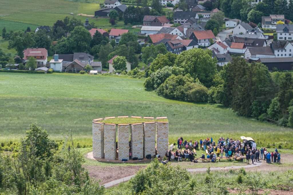 A community gathering outside the Open Chapel in Hillerhausen with people sitting on benches during a public event.
