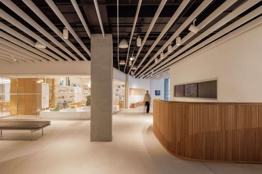 Minimalist reception area at Gardiner Museum featuring a curved oak wood desk and linear ceiling baffles.