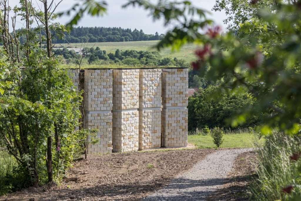 Close-up of vertical sandstone columns of the Open Chapel with a gravel path leading towards the structure.