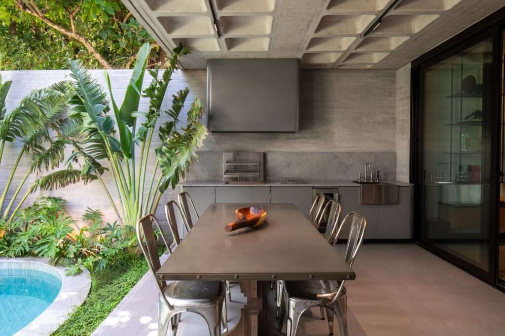 Outdoor dining area at Casa Refugio featuring a concrete waffle slab ceiling, industrial table, and integrated barbecue station.