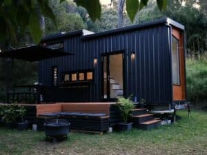 Exterior view of the Currumbin tiny home by Removed Tiny Homes featuring black corrugated metal cladding and a wooden deck.